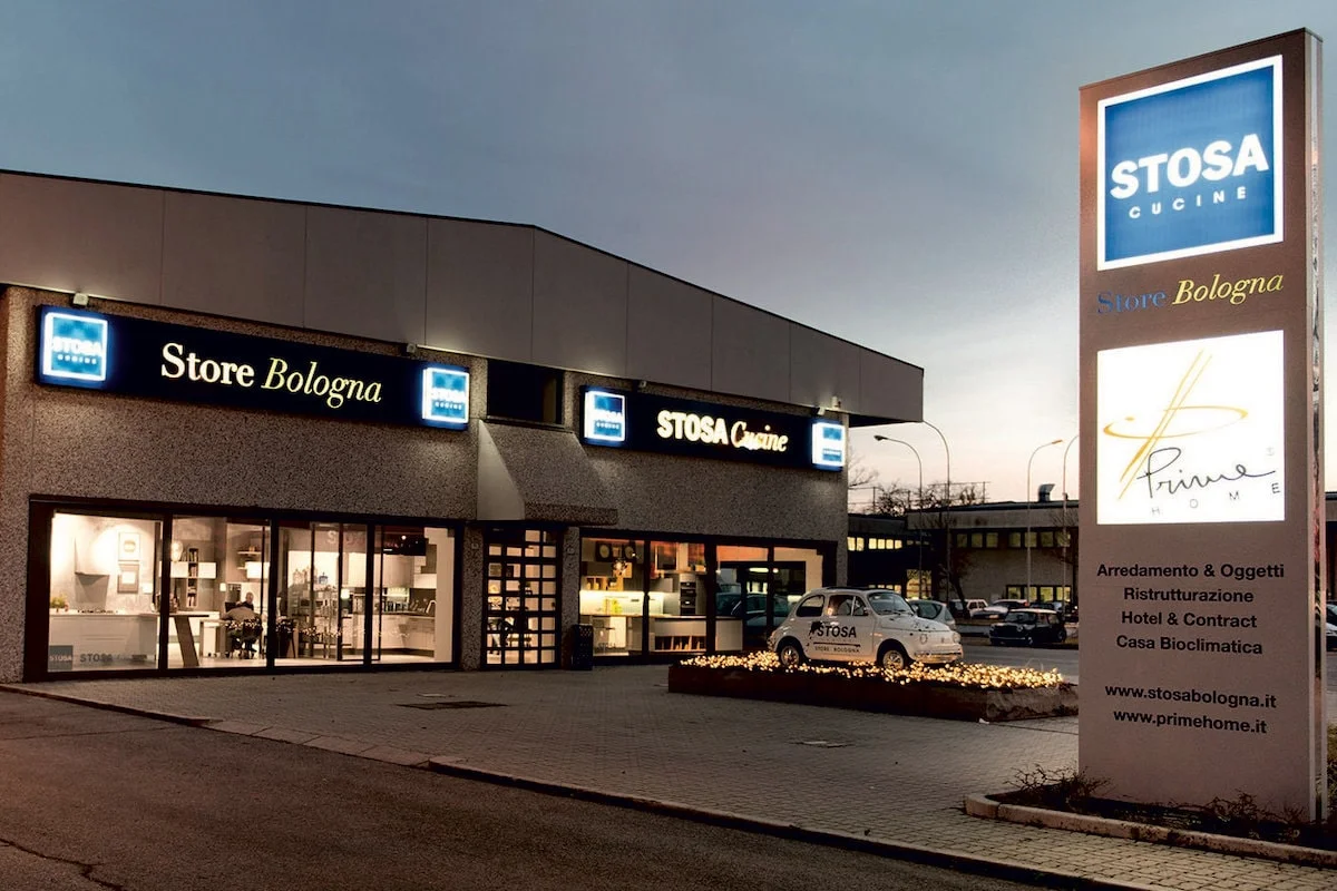 Lo showroom Stosa Cucine Store Bologna visto dal piazzale, di sera, con le insegne e le vetrine illuminate